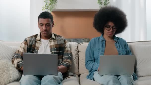 アフリカ系アメリカ人の女性は 自宅で働いている2人のフリーランスと自宅で働いている2台のPcコンピュータとラップトップマンの仕事でオンラインで働いていますリビングルーム技術中毒隔離家族 — ストック動画