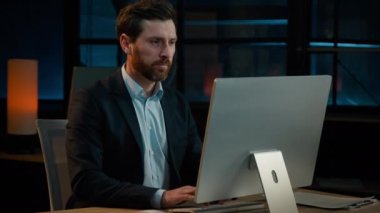 Beyaz iş adamı, 40 'lı yaşlarda, erkek, yetişkin, yönetici, akşam ofisinde gülümseyen, bilgisayar e-ticaret sitesinde iş verileri üzerinde çalışan, internet sitesinde tatmin olmuş gülümseyen.