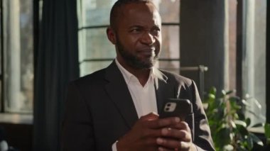 Olgun 40 'lı yaşlardaki Afro-Amerikan etnik erkek işadamı cep telefonuna e-posta yazmayı düşünüyor.