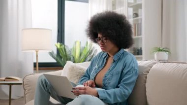 Endişeli Afrikalı Amerikalı kadın dizüstü bilgisayarla stresli umutsuz şokla üzgün üzgün kötü haberleri okuduğu için üzgün. Evdeki kanepe kızlarının bilgisayarlarında kaybolan kötü haberleri okuduğu için endişeli mali sorunlar.