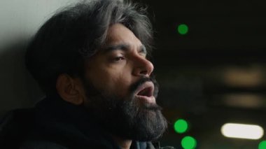 Çaresiz, evsiz, bunalımlı, stresli, sakallı adam karanlık otopark gecesinde acı çekiyor. Arap, stresli, kederli, üzgün adam nefesini tutuyor. Soğuk, dumanlı, dumanlı, soğuk hava bacası soluyor.
