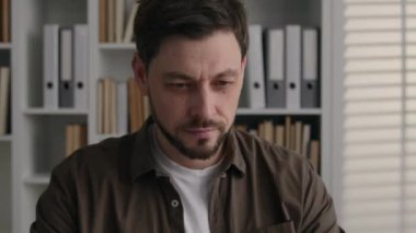 Düşünceli, düşünceli, beyaz bir adam ofiste dizüstü bilgisayarla çalışıyor. Erkek yazar, gazeteci, tasarımcı, işadamı, iş adamı. Düşünüp taşınan derin düşüncelere dalın.