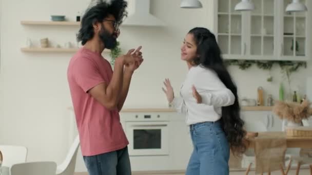 有趣的一对多种族的女人和男人在厨房里跳舞精力充沛的疯狂舞动阿拉伯印第安舞女和男人搬去音乐家庭派对庆祝周末搬到新房子 — 图库视频影像