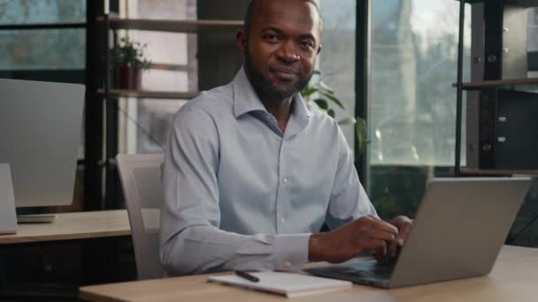 成熟したシニアアフリカ系アメリカ人男性40代の中年ビジネスマンは オフィス企業のビジネス会社でオンラインでラップトップコンピュータのタイピング電子メールネットワークチャットカメラの笑顔を見て座っている — ストック動画