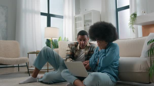 非洲裔美国人夫妇坐在自家客厅的地板上女人妻子很伤心遭受着笔记本电脑错误的困扰网上坠机失恋男人帮助平静下来帮助支撑 — 图库视频影像
