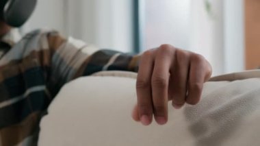 Hareketli çekim mutlu barışçıl Afrikalı Amerikalı adam rahat koltukta dinleniyor kablosuz kulaklıkla müzik dinliyor tembelce haftasonu şarkıları söyleyerek evde yalnız başına şarkı söylüyor.