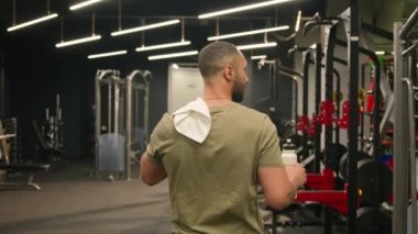 Afrika kökenli Amerikalı erkek, kaslı spor antrenörü spor kulübü eğitmeni, omuzlarında havluyla Latin sporcu boksör egzersiz sonrası spor salonunda su içerek yürür.