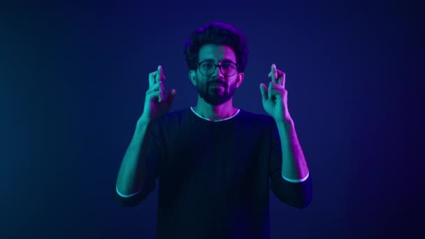 希望に満ちた強調絶望的なインドの男性コーダープログラマーコンピュータ技術労働者の指が祈りを越え勝利の幸運を祈るジェスチャー希望を作る青ネオンスタジオの背景 — ストック動画