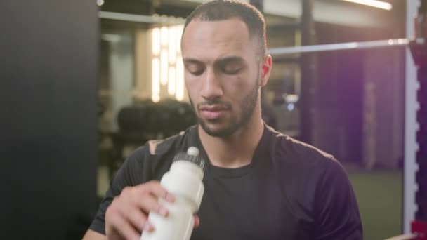 疲惫不堪的非洲裔美国运动员男人在健身房锻炼时喝蛋白质补充运动健身瓶中的水疲惫不堪的男性健美运动员在运动后笑着喝着提神 — 图库视频影像