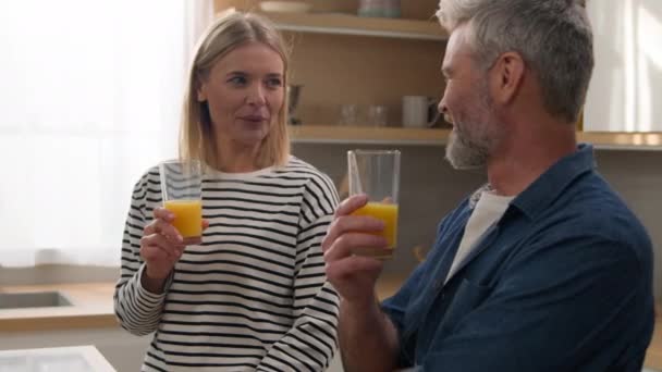 大人中年カップル白人男性女性配偶者幸せな家族でキッチンで飲むオレンジジュースカジュアルな会話トークドリンク新鮮な健康的な栄養食事配達サービス医療 — ストック動画