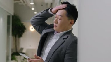 Ofisteki Asya 'lı yorgun etnik adam cep telefonu taşıyor. Kore' li üst düzey Japon iş adamı. Bozuk akıllı telefon sahibi üzgün.