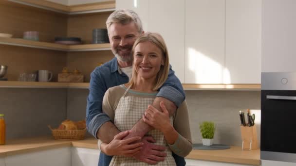 幸せな家族気楽なカップル大人中年の配偶者シニア男と成熟した女性の家の所有者抱きしめるキッチンで笑顔で調理した後新鮮な野菜サラダ一緒に家の肖像画 — ストック動画