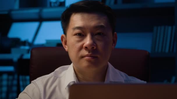严肃的亚洲企业家雇主韩国商人在办公室深夜在网上打字的笔记本电脑大人们沉着冷静的中国男人日本男性经理电脑操作看着相机肖像 — 图库视频影像