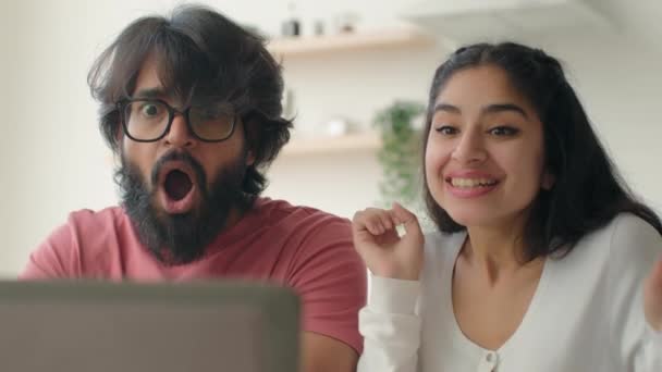 幸せなカップル多人種アラビア人の男性と女性と紙はキッチンでラップトップ画面上で見るオンラインオファー住宅ローン承認ローンクレジット民族の女の子男は高い5を与える勝利の達成を祝う — ストック動画