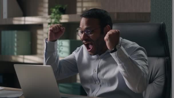 大声で叫んで不思議インドのビジネスマンアメリカの男性のラップトップの勝利賭け興奮信じられないほど良いニュースオフィスでオンライン成功を達成幸せな感情的なエグゼクティブ勝利コンピュータを叫んで — ストック動画