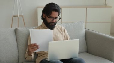 Hintli Arap Müslüman iş adamı ev bilgisayarından iş bilgisayarı okuyor. Evrak ipoteği vergisi, sigorta, serbest çalışan bir erkek. Finansal evrakları kontrol ediyor.