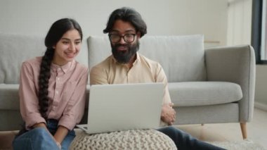 Çok ırklı bir çift olan Arap erkek ve Hintli aile fertleri ev sahibi çift ev sahibi karı koca sevgili dizüstü bilgisayarda film izleyen sevgili akıllı televizyon keyfi, gülümseme, konuşma videosu, gülümseme, gülücük.