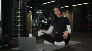 Kadın spor eğitmeni Kafkas kadın havluyla ter silme sporcusu kız spor salonundaki spor salonunda spor salonunda dijital aletler üzerine eğitim videosu yogası öğretiyor.