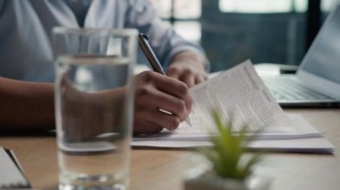 Sınav kağıtlarını ofis masasında bir bardak suyla bitiren erkek eli kapat. Kağıt notlar yazan iş adamı tanınmayan bir öğrenci. Belge metni, sigorta özeti.