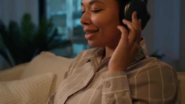 リラックスしたアフリカ系アメリカ人女性笑顔ビジネス女性から働くホームタイプのラップトップ勉強オンライン民族の女性の女の子は 音楽のメロディーを聞きます高品質の音でヘッドフォンリラックス夜遠くの仕事 — ストック動画