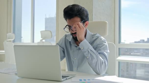 疲れたアラビア系インド人男性ビジネスマンは痛みを伴う頭目の疲れを感じる男性の病気の従業員オフィスで過労ラップトップの仕事は 眼鏡のメッセージをオフに取ります乾燥した目の悪い視力視力視力の健康問題 — ストック動画