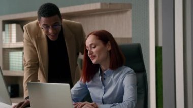 Afrikalı Amerikalı iş adamı koçu, bilgisayar öğretmeni stajyer iş kadınına bilgisayardaki projeyi açıklarken yardımcı oluyor. Gülümseyen kadın ve erkek iş arkadaşları iş birliği yapıyor.