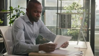 Sinirli, yorgun, yetişkin iş adamı Afro-Amerikalı olgun 40 'lı yaşlardaki adam notlar yazıyor. Kağıt belgeler okuyor. Yorgun, hasta, erkek çalışanı güneş ofisinde oturuyor.