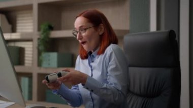 Komik kadın ofis çalışanı video oyunu bağımlısı konsol kumandanı kadın çevrimiçi oynarken kimse kız iş kadınının yakalanmaktan korktuğunu görmüyor oyun çubuğunu saklarken bilgisayarla çalışıyormuş gibi yapıyor.