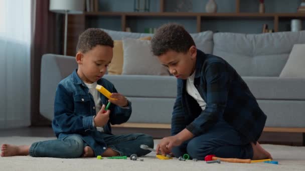 2人の子供の男の子小さなアフリカ系アメリカ人の子供の民族の友人の兄弟は プラスチック製のおもちゃを修復する演奏ドライバーと修理ゲーム リビングルームの自宅で床で楽しい時間を過ごすスパナーレンチ — ストック動画