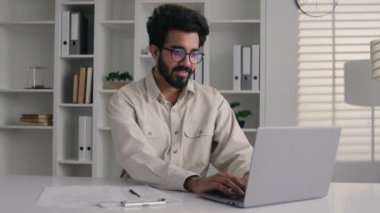 Yorgun Hintli Müslüman iş adamı hasta erkek ofis girişimcisi dizüstü bilgisayar işi sırasında omurga spazmı masajı yapan hasta adamın sağlık sorunu yüzünden sırt ağrısı çekiyor.