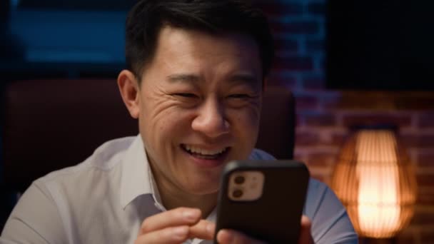 幸せなアジアの中年男性夜の家のオフィスで韓国の大人のビジネスマンは 携帯電話を使用して笑い笑いユーモラスなビデオで面白いユーモアを持っているスマートフォンオンラインアプリのソーシャルメディア — ストック動画