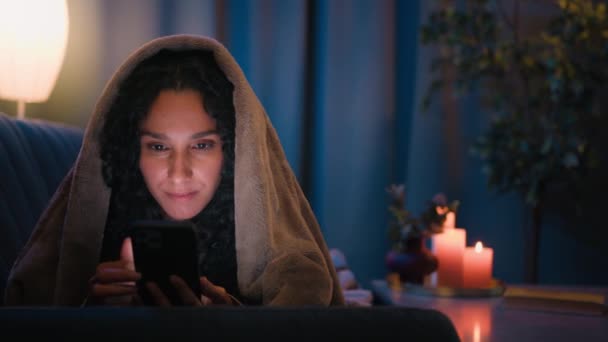 ヒスパニック系アラビア人の女の子ラティノ女性インド人中毒女性で夜の家でベッドの下に毛布カバーとともにDuvet見る携帯電話スクロールブラウジングソーシャルメディアスマートフォンインフルエンサー中毒ガジェット — ストック動画