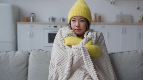 冷凍アジアの中国人韓国人女性病気悲しい女の子凍結座って寒さのアパートで苦しむ低温凍結カバー暖かい毛布帽子とミトン冬の季節の暖房問題で家庭キッチン — ストック動画