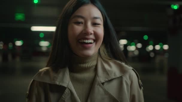幸せなアジアの女性笑って誠実な笑顔のポートレート中国の日本人の女の子のおもちゃの笑顔の女性の暗い駐車場でカメラを見て笑う面白い冗談楽しい喜び陽気な感情良いニュース — ストック動画