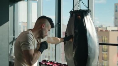 Spor eldivenleriyle boks şampiyonu yorgun erkek boksör boksör boksörleri kum torbasına vuruyor. Beyazlı sporcu spor salonunda yumruk kutusuna vuruyor. Spor kulübünün spor salonunda yumruk atıyor.