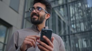 Arap erkek ticareti girişimcisi Hintli Müslüman iş adamı şehir caddesinde mobil uygulama kullanarak akıllı telefon sosyal medya bağımlısıyla sohbet ediyor mutlu erkek ofis müdürü telefon ekranında gülümsüyor