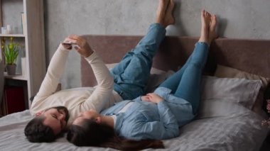 Kafkasyalı rahat bir aile erkek ve kız arkadaş yatak odasında bacakları üzerinde uzanan cep telefonlu bir film izleyip rahatlayıp internetten alışveriş yapan bir erkek ve kız arkadaş.