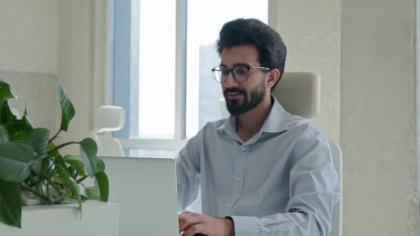 アラビア語インドの実業家のプロの起業家ソフトウェアエンジニアの雇用主は オフィスの職場でノートパソコンでビジネスプロジェクトのスタートアップを入力すると カメラの笑顔を見て幸せなイスラム教徒の男 — ストック動画