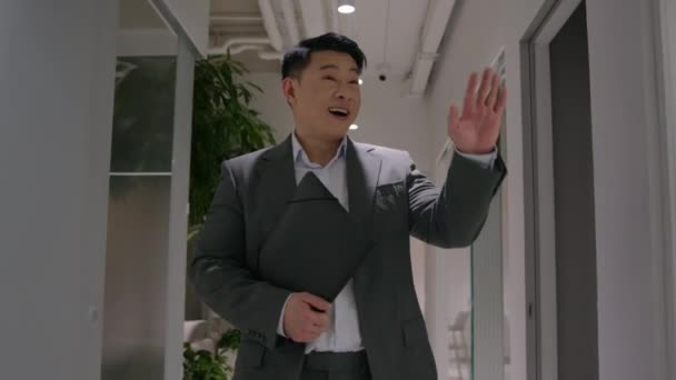 オフィスの廊下を歩く幸せなアジアの中高年ビジネスマンは 廊下で同僚を迎える中国の男性リーダーのCeoの会社は職場を離れる笑みを浮かべて文書でビジネスミーティングのフォルダに移動します — ストック動画