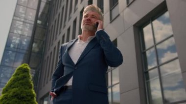 Orta yaşlı iş yatırımcısı yetişkin girişimci kıdemli işadamı şirket binası yakınında telefonla konuşan yetişkin işveren. Cevap görüşmeleri. Cep telefonu görüşmeleri. Proje anlaşması hakkında konuş.