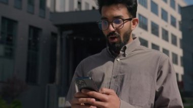 Heyecanlı Hintli işadamı dışarıda cep telefonu kullanıyor. Şok olmuş Arap erkek işvereni kazandı. Akıllı telefon bahsini kazandı.