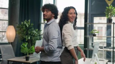 İki iş ortağı çok ırklı Arap erkek işadamı ve İspanyol kadın iş kadını ofis yöneticileri ve takım liderleri gülümseyerek iş birliği yapıyor.