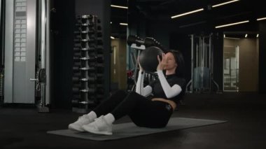 Beyaz tenli sporcu kadın güçlü kaslı kadın fitness antrenörüne uyuyor. Spor topu atıyor. Spor salonunda spor aletleri kullanıyor.