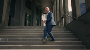Mutlu Kafkasyalı kıdemli iş adamı yetişkin işadamı iş adamı dans ediyor ofis binasının yakınındaki merdivenlerde yürüyor hareketli dans başarısı zaferi kutluyor eğlencenin tadını çıkarın