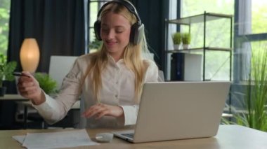 Kaygısız gülümseyen Kafkasyalı kadın kulaklıkla müzik dinliyor müdür kız sekreter şarkıya geçiyor kulaklıktaki sesin keyfini çıkarırken internetten iş kadını bilgisayarında çalışıyor ofiste evrak işleri yazıyor.