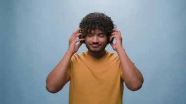 Stüdyo portresi mutlu Arap erkek. İspanyol erkek kulaklık takmış. Müzik dinliyor, radyoda mavi arka planda şarkı söylüyor.