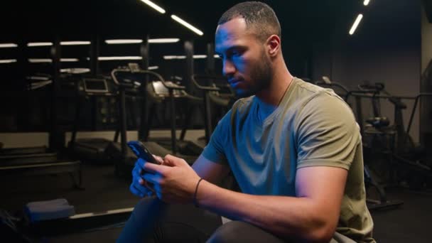 非裔美国人健美运动员私人教练使用智能手机运动员在社交媒体上浏览在线信息手机分享锻炼照片在健身房在线体育应用服务 — 图库视频影像