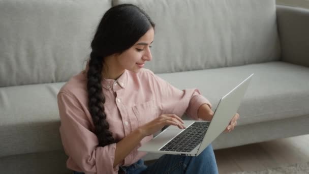 自由撰稿人微笑阿拉伯裔印度姑娘在地板上工作的女商人在笔记本电脑上打字留言在线浏览社交媒体快乐的顾客让网上定单递送微笑 — 图库视频影像