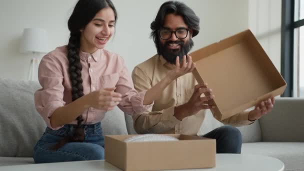 一对快乐的夫妇顾客收到包裹看里面的盒子阿拉伯印度男人和女人打开送货兴奋的丈夫和妻子在网上购物打开盒子买东西拆包礼物让网上订货单买东西 — 图库视频影像