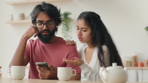 不安は 携帯電話を見てキッチンでインドのアラビア人のカップルの住宅所有者を強調悪いニュース銀行の電子メールは モバイルアプリの障害問題スマートフォンのトラブルを使用して住宅ローンの多様な女性と男性を拒否 — ストック動画
